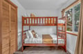 Your cozy bunk room features rich wood furniture and crisp linens, creating a comfortable retreat with natural light streaming through large windows.