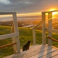 A dramatic coastal sunset illuminates the rugged landscape, with white wooden deck railings framing the golden hour scene near this oceanfront retreat.