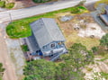 Aerial view of a charming coastal retreat featuring spacious grounds, wraparound deck, and convenient parking area.