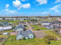 Aerial view of coastal community featuring residential buildings spread across green fields with water visible in the distance.