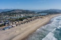 Stunning aerial view captures a pristine coastal community with expansive sandy beach meeting Pacific waves, surrounded by forested hills and residential neighborhoods.
