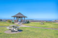 Coastal pavilion with picnic area overlooking pristine beach and tidal flats under expansive blue sky.
