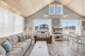 Relax in your airy living room with vaulted wood ceilings, cozy seating, and coastal light streaming through large windows. The open layout invites you to unwind after a day exploring nearby beaches.