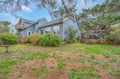 Charming blue cottage nestled among mature trees with a spacious yard and wooden deck areas.