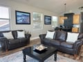 Sink into plush leather sofas and unwind in your open-concept living space. Abundant natural light streams through large windows while thoughtful coastal artwork sets a relaxed, welcoming tone for your getaway.