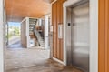 This shared outdoor hallway leads to your unit, featuring convenient elevator access and a glimpse of the surrounding neighborhood through the open walkway.