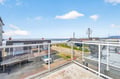 Modern balcony with glass railings overlooking coastal neighborhood and distant ocean views under bright blue skies.