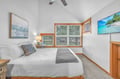 Drift off to peaceful sleep in your bright bedroom with crisp linens, natural light streaming through large windows, and tropical artwork setting the mood.