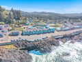 Aerial view of a charming coastal town nestled between forested hills and dramatic rocky coastline with pristine blue waters.