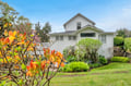 Charming white cottage nestled among vibrant blooming azaleas and manicured gardens under clear blue skies.