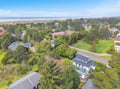 Aerial view of coastal neighborhood with tree-lined streets leading to sandy beach and ocean waves.