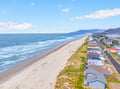 Expansive coastal community stretching along pristine sandy beach with rolling waves and mountain backdrop.