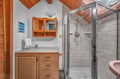 Step into your private bathroom featuring warm wood accents, a refreshing glass-enclosed shower, and charming vaulted ceilings that create an airy, cabin-like retreat.