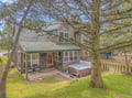 A charming coastal cottage with natural cedar siding and a private hot tub nestled among mature trees.