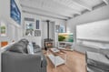 Cozy up in this charming cottage living room with crackling fireplace, coastal artwork, and modern entertainment setup for perfect seaside relaxation.