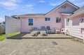 Cheerful pink cottage with a private patio area featuring lounge chairs and outdoor seating, perfect for relaxing in the coastal sunshine.