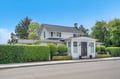Charming white cottage with manicured hedges and classic architecture creates an inviting streetside presence in a peaceful neighborhood setting.