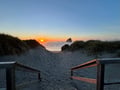 A stunning sunset over the ocean showcases the dramatic coastline near the property, with sandy dunes and a distinctive rock formation creating a picturesque coastal setting.