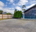 Ample paved parking area provides easy access to the property, with mature evergreens and a bright blue sky overhead.
