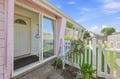 Charming pink and white exterior with a private garden and white picket fence. This sunny property features a welcoming entrance surrounded by lush greenery and blooming flowers.