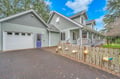 A charming coastal-style home with sage green siding and a welcoming front porch, featuring convenient driveway parking behind a rustic fence.