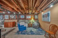 Relax in your unique basement lounge featuring exposed wooden beams, eclectic artwork, and comfortable seating for memorable evenings.