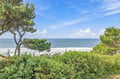 A coastal scene featuring lush greenery, sandy shores, and rolling waves under a bright blue sky—a peaceful backdrop to the surrounding property area.
