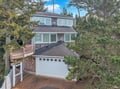 Charming cedar-shingled home nestled among towering pines, featuring multiple levels and a welcoming wooden deck for coastal relaxation.