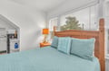 Drift off in your cozy bedroom with warm wood furnishings, cheerful beach-themed decor, and natural light streaming through large windows.
