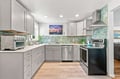 Step into your fully-equipped kitchen featuring soft gray cabinetry, gleaming stainless steel appliances, and spa-inspired aqua tile backsplash that catches the light beautifully.