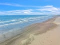 Pristine sandy shoreline stretches endlessly under brilliant blue skies, with gentle waves creating the perfect coastal escape.