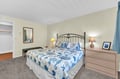 Drift into peaceful sleep on your comfortable queen bed with coastal-themed linens, warm bedside lighting, and convenient dresser storage.