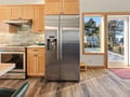Cook your meals in this spacious kitchen featuring stainless steel appliances, warm wood cabinetry, and windows overlooking leafy treetops.
