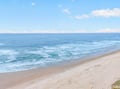 Pristine sandy beach stretches along crystal-clear waters under a brilliant blue sky with gentle waves lapping the shore.