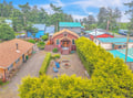 Aerial view of the property nestled in a residential neighborhood, showcasing the main building, landscaped yard with fire pit seating, and surrounding tree-lined area.