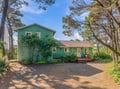 A charming coastal retreat nestled among towering pines, featuring a welcoming front deck and gravel parking area perfect for your seaside getaway.