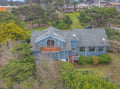 Aerial view of charming blue coastal home nestled among lush trees in peaceful residential neighborhood.