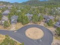 Aerial view of a coastal residential community with forested hills and vacation homes surrounding a circular cul-de-sac.