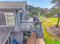 Charming coastal cottage with multi-level deck and BBQ grill, surrounded by mature trees in a peaceful neighborhood setting.