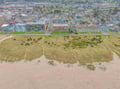 Aerial view of coastal property buildings positioned along sandy beach with natural dunes and residential neighborhood backdrop.