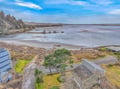 Aerial view of beachfront property nestled between forested coastline and pristine sandy shores with rocky outcroppings in calm waters.