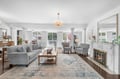 Your elegant living room awaits with plush gray seating, warm fireplace, and crystal chandelier creating the perfect atmosphere for relaxation.