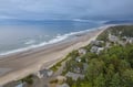 Stunning aerial view reveals a pristine coastal community where rolling waves meet expansive sandy shores, nestled among verdant forest bluffs.