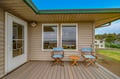 This covered deck offers a private spot for morning coffee with two director's chairs and a side table, overlooking a quiet residential neighborhood with coastal views.
