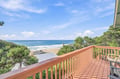 Step out onto your private balcony and breathe in the ocean breeze as waves roll gently onto the sandy shore below, framed by coastal pines under endless blue skies.