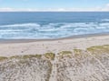 Pristine sandy coastline stretches along rolling ocean waves under a partly cloudy sky.