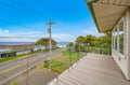 A spacious deck overlooks the coastal road, offering glimpses of the ocean beyond windswept trees—a peaceful spot to watch the day unfold.