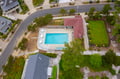 Aerial view of property featuring a sparkling swimming pool surrounded by landscaped grounds and mature trees in a quiet residential neighborhood.