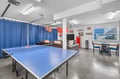 Challenge friends to ping-pong in this vibrant entertainment space. Blue curtains divide the room, while fun vintage signs and a flat-screen create a casual hangout atmosphere with dining and lounge seating nearby.