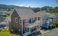 Two-story coastal cottage with wrap-around balconies set in a hillside neighborhood surrounded by lush trees and mountain views.